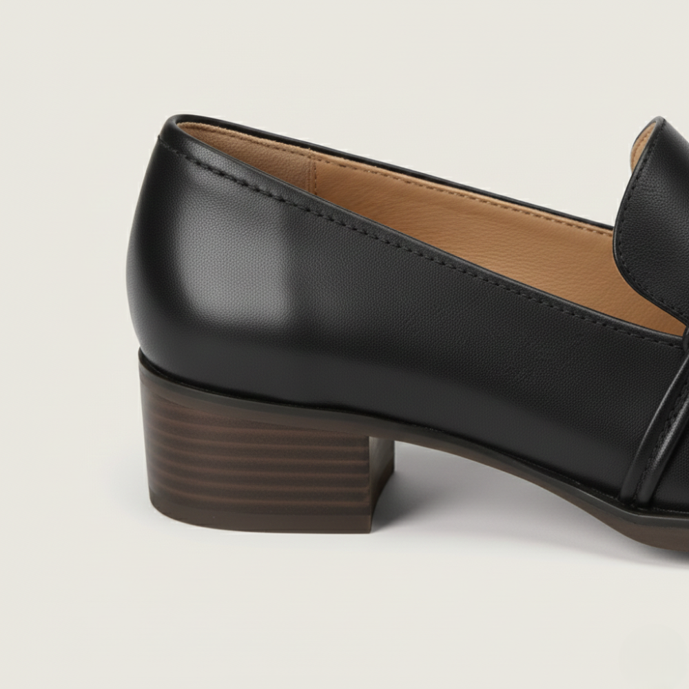 Black leather loafers for women with a brown block heel on a light beige background